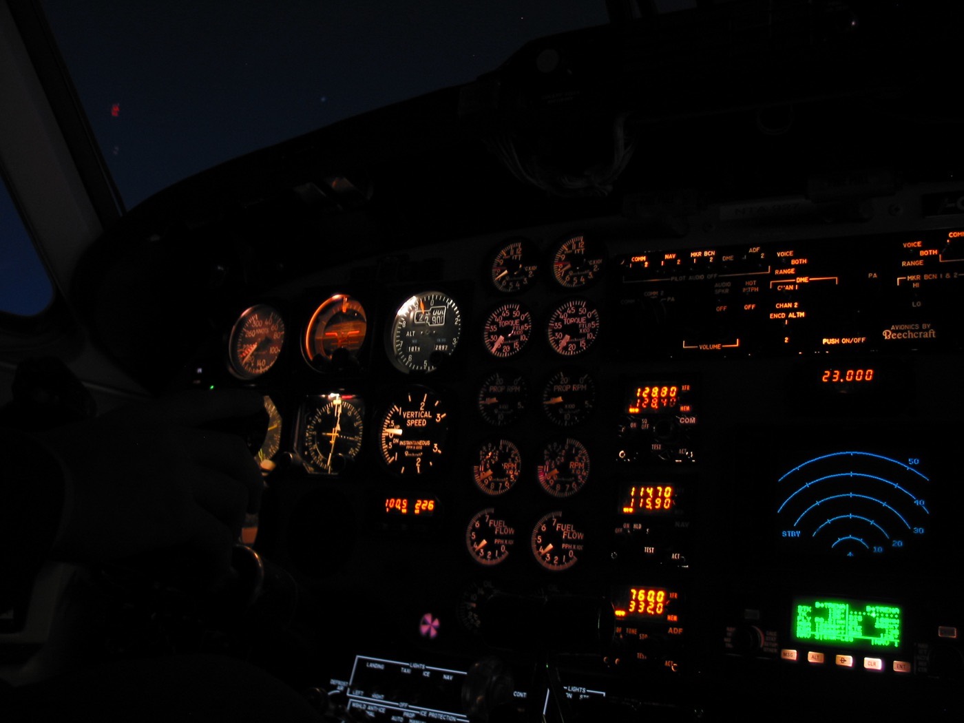 Planche de bord d'un avion éclairée en rouge/orangé de nuit, ciel sombre visible à travers le pare-brise